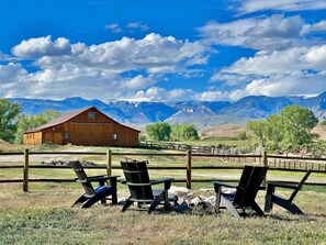A wooden barn with a fenced area, three Adirondack chairs, and a mountainous landscape in the background. - Wheels Up Cottage at Ever Sky Ranch, THE VIEWS! (Shell)