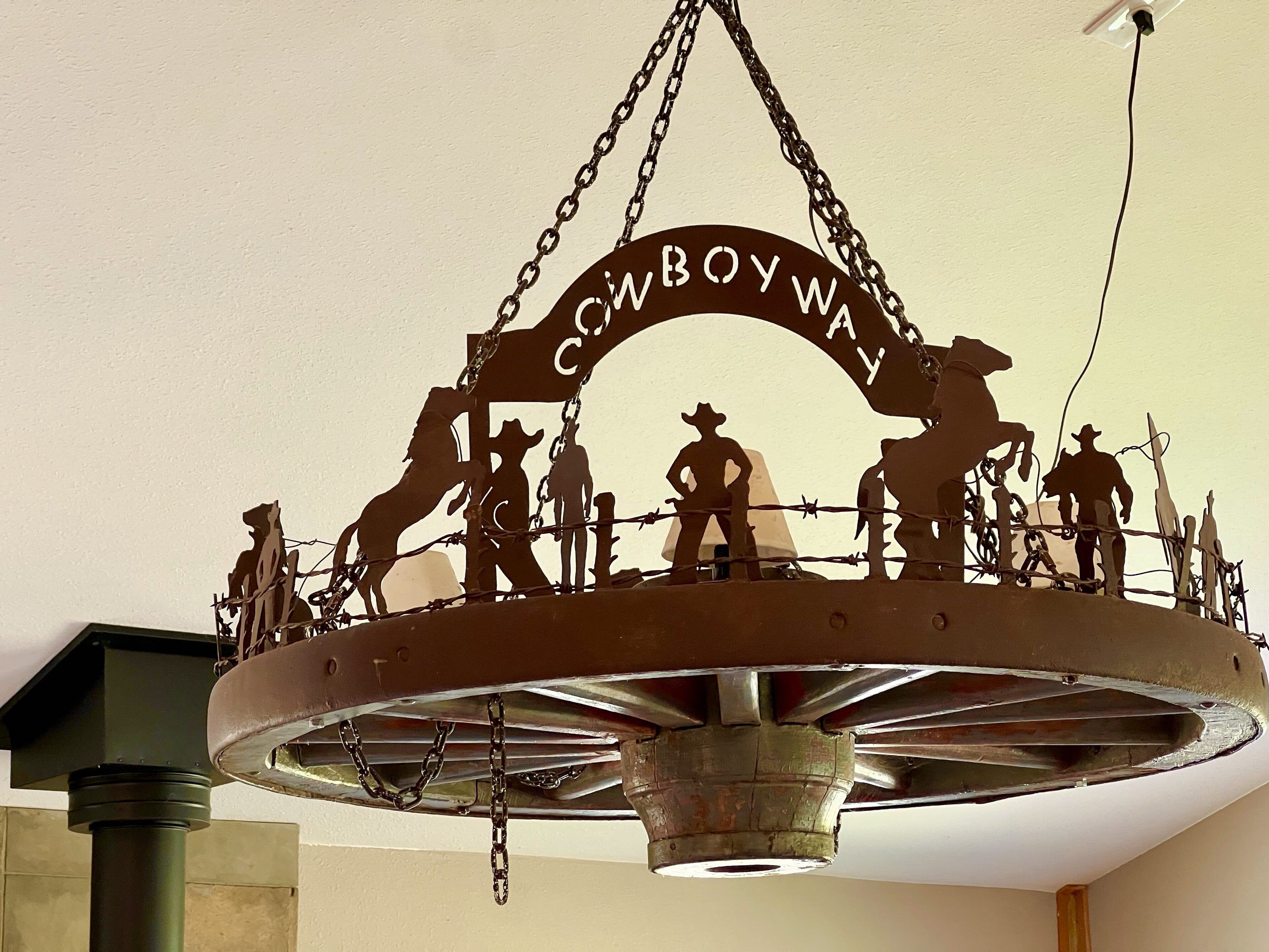 Escultura de metal retratando cowboys e cavalos, com o texto "Cowboy Way" no teto.