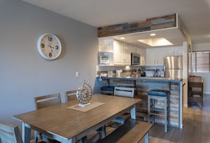 A modern kitchen with white cabinets, a stainless steel refrigerator, and a wooden dining table with chairs.