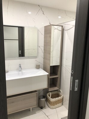 A modern bathroom with a white marble wall, a large mirror, a white sink, and a wooden cabinet.