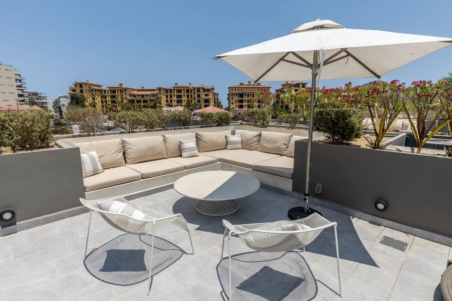 Eine Dachterrasse mit einem beigefarbenen Ecksofa, zwei Korbstühlen, einem runden Tisch und einem großen Sonnenschirm.