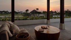 Een gezellig buiten zitgedeelte met een ronde houten tafel, een comfortabele bank en een rieten mand.