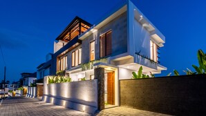 Een modern huis met twee verdiepingen, een goed verlichte ingang, een balkon en een verharde oprit.