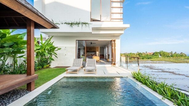 Een modern huis met een zwembad, twee ligstoelen en uitzicht op de oceaan.