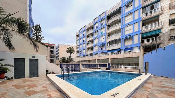 A swimming pool with a tiled deck, surrounded by a multi-story building with balconies. - Welcoming seafront apartment Tv15 (Torrevieja)