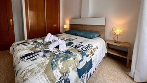 A hotel room with a large bed, wooden headboard, two bedside lamps, and a wardrobe. - Welcoming seafront apartment Tv15 (Torrevieja)