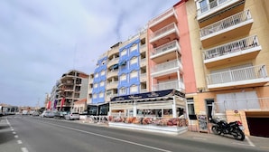 A street view with a blue and pink building, a restaurant named 'Grillhouse', and a parked motorcycle. - Welcoming seafront apartment Tv15 (Torrevieja)