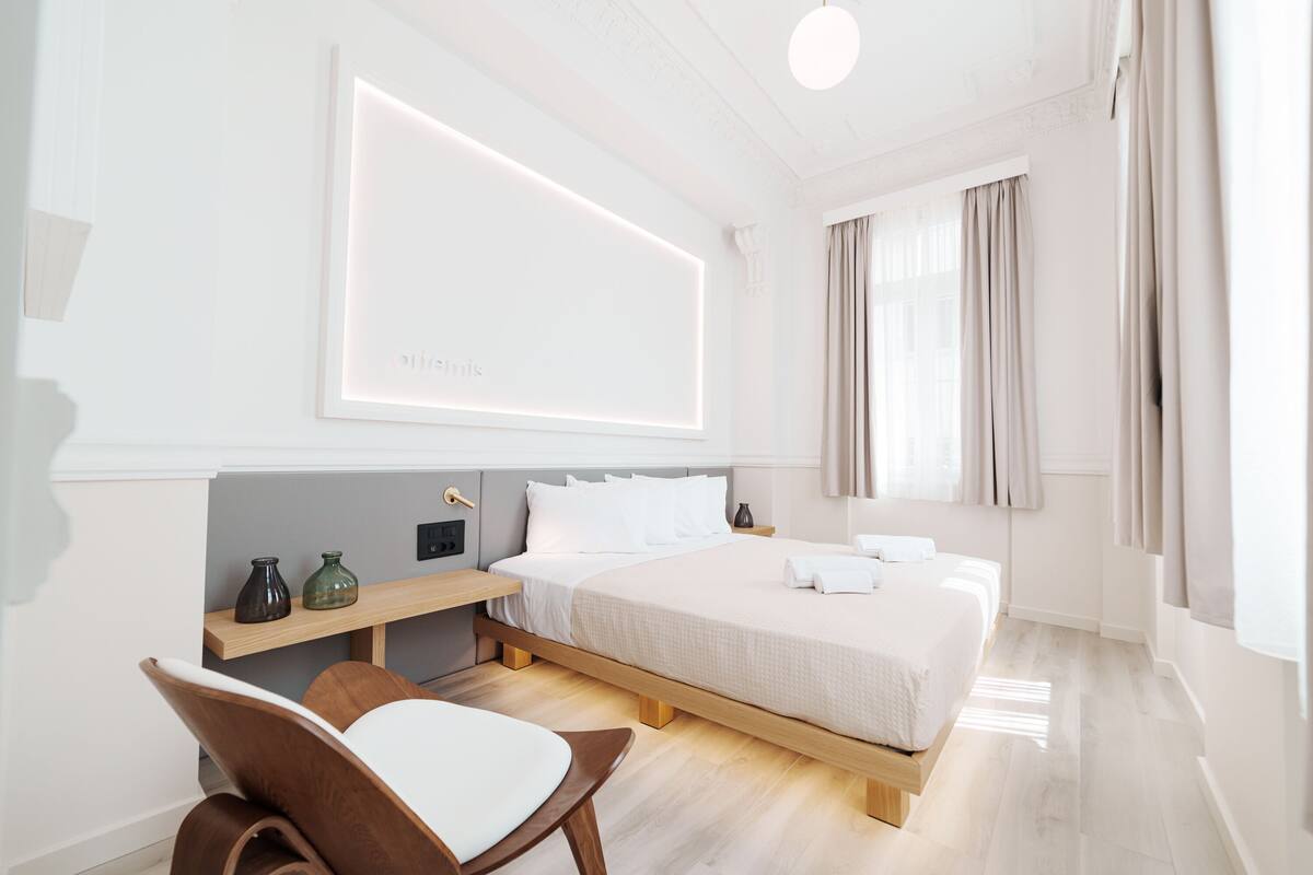Een moderne hotelkamer met een groot bed, nachtkastjes, een stoel en een tv aan de muur.