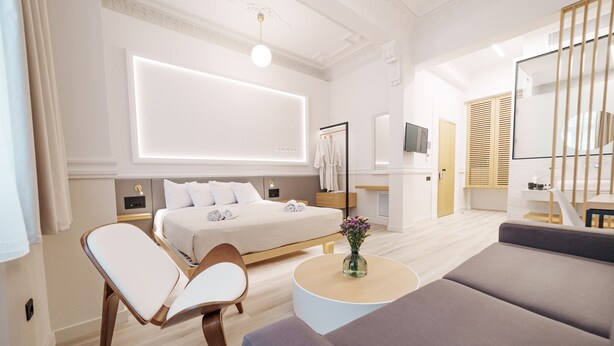 A modern hotel room with a large bed, a sofa, a chair, a round coffee table, and a TV. - Agora Athens Suites (Athens)