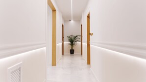 A modern hallway with white walls, wooden door frames, and a central potted plant. - Agora Athens Suites (Athens)