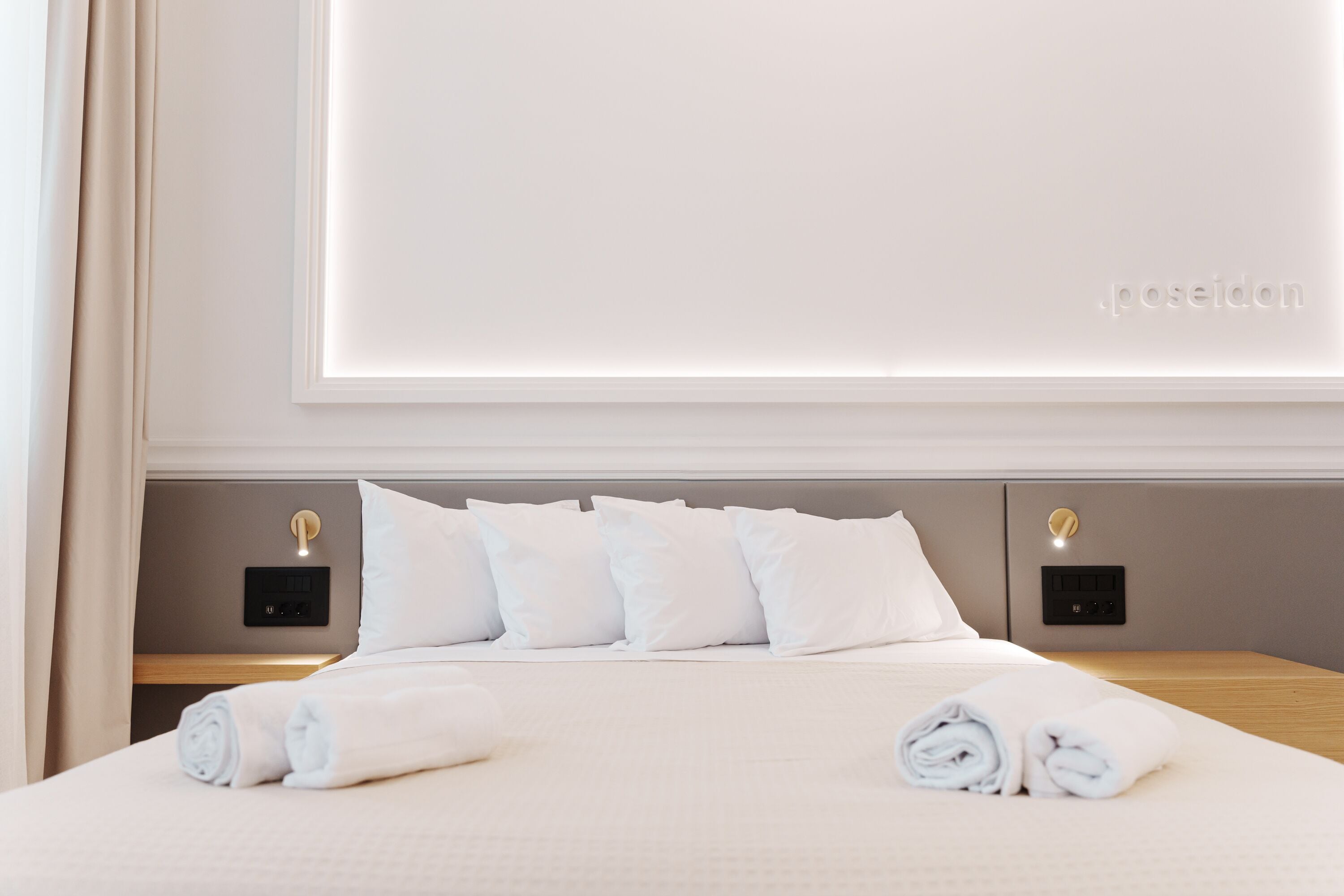 Una cama bien hecha con sábanas y almohadas blancas, una mesita de noche con lámpara y un panel de control en la pared.
