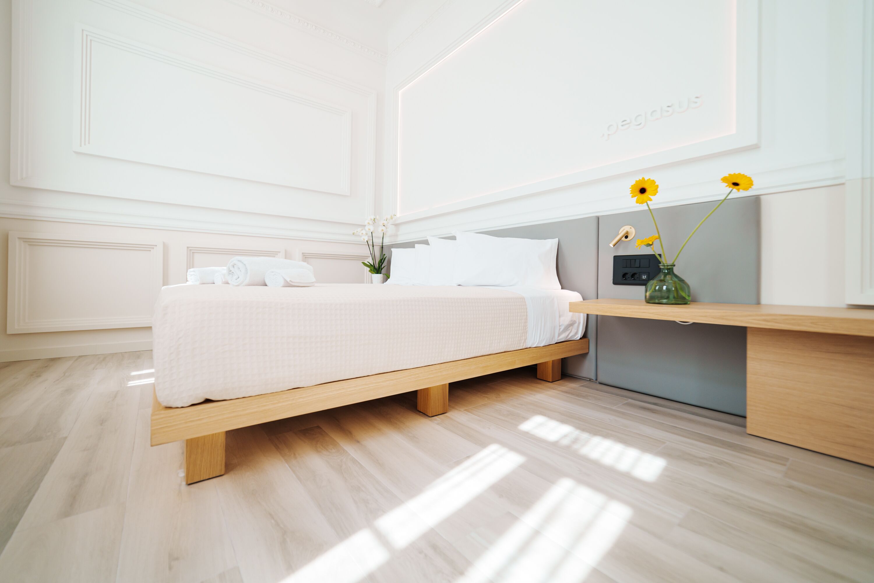 A modern bedroom with a wooden bed, white bedding, a bedside table, and a vase with flowers.