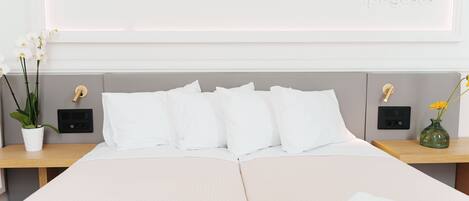 A neatly made bed with white linens, a bedside table with a vase of flowers, and a wall-mounted light switch.