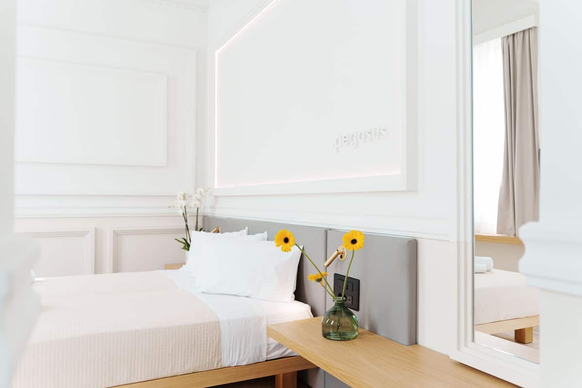 Een hotelkamer met een bed, een nachtkastje met een bloemenvaas en een spiegel aan de muur.