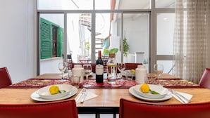 Een gedekte eettafel met borden, bestek, glazen en een fles wijn, met uitzicht op een wenteltrap en groen buiten.