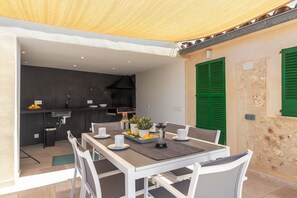 Un coin repas avec une table dressée pour quatre personnes, une cuisine en arrière-plan et un balcon doté d’un auvent en bois.