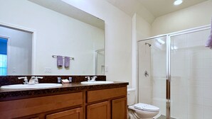 Un baño con dos lavamanos, un inodoro y una ducha con mampara de vidrio.