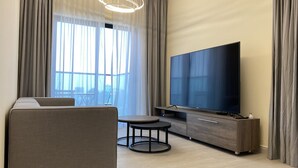 Moderni olohuone, jossa on sohva, pyöreä pöytä, litteänäyttöinen televisio ja suuri ikkuna, jossa on verhot.