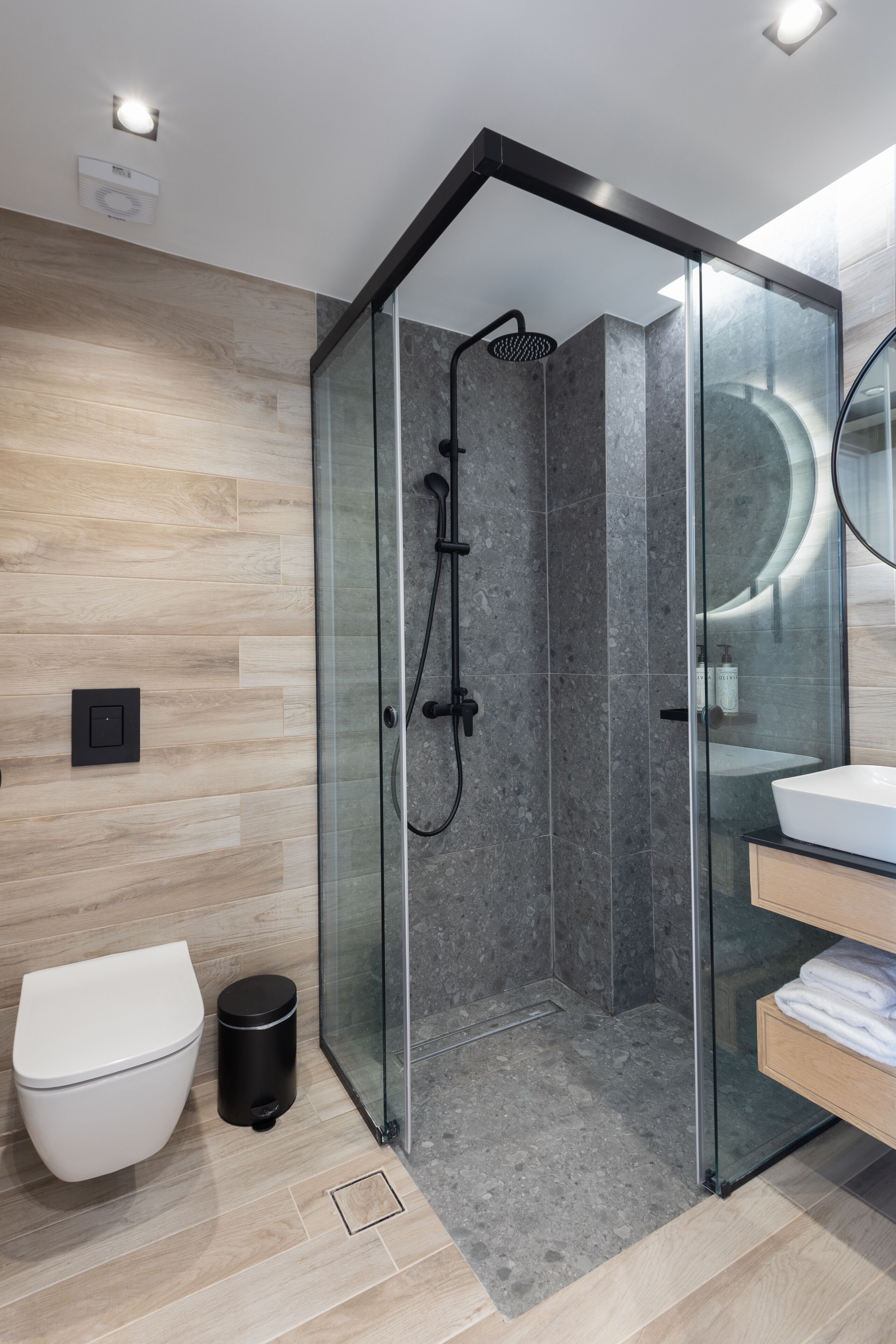 A modern bathroom with a glass-enclosed shower, a white toilet, and a wooden vanity with a sink.