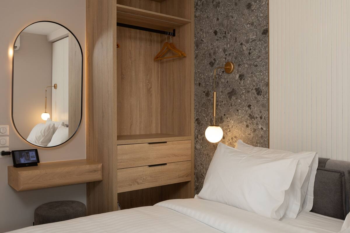 Un dormitorio con cama, mesita de noche, espejo, armario y lámpara colgante.