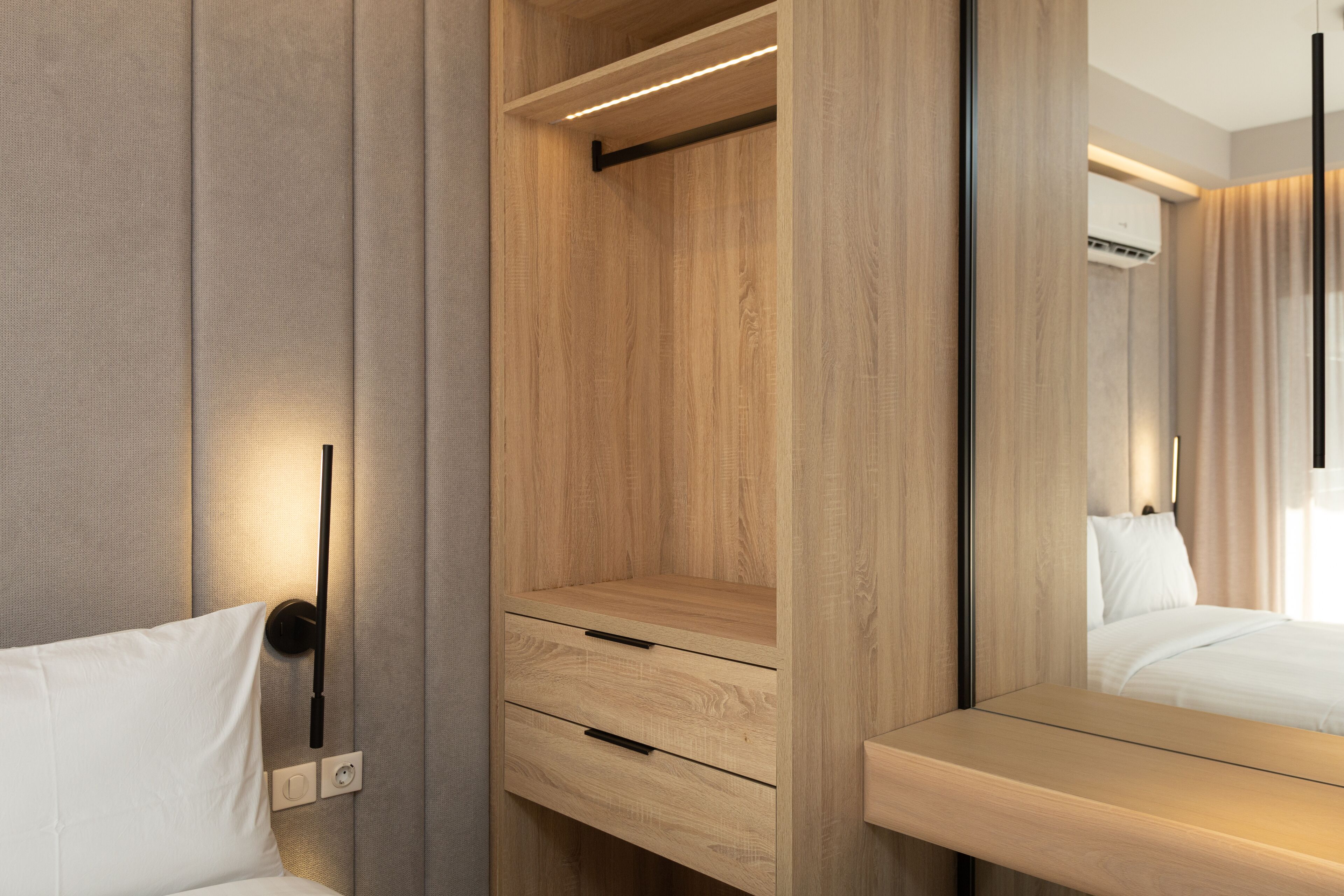 Moderni hotellihuone, jossa on puinen vaatekaappi, yöpöytä ja suuri peili.