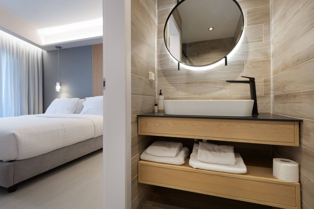 Una habitación de hotel moderna con una cama, un baño con un espejo redondo, un lavabo y toallas.