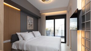 A modern bedroom with a large bed, a flat-screen TV mounted on the wall, and a view of the city through the window. - LUX&EASY Athens Downtown Residences (Athens)