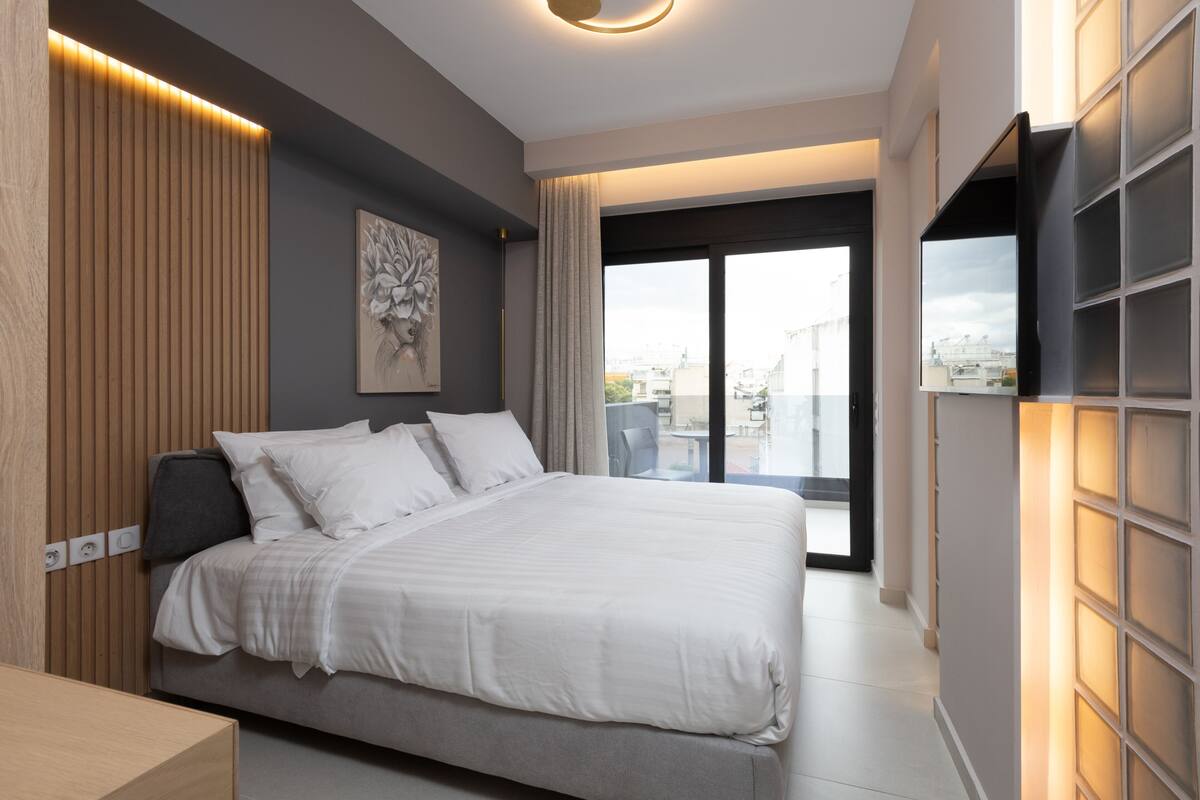 Un dormitorio moderno con una cama grande, un televisor de pantalla plana en la pared y vistas de la ciudad por la ventana.