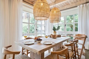 Un comedor con mesa de madera, sillas de mimbre y un ventanal con vistas a la vegetación.