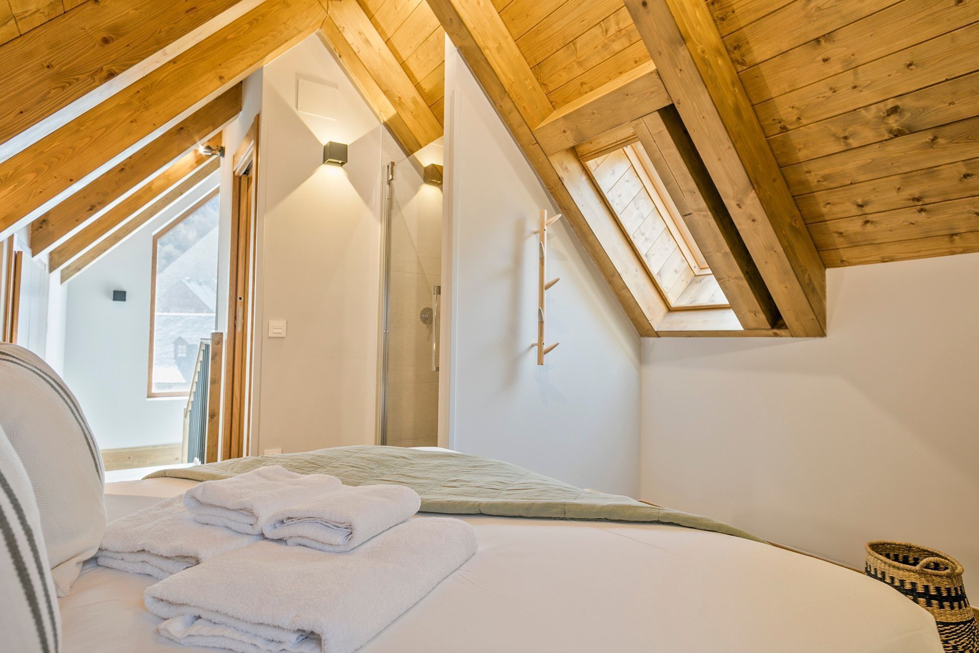 A bedroom with a sloped ceiling, a skylight, a bed with neatly folded towels, and a small woven basket.