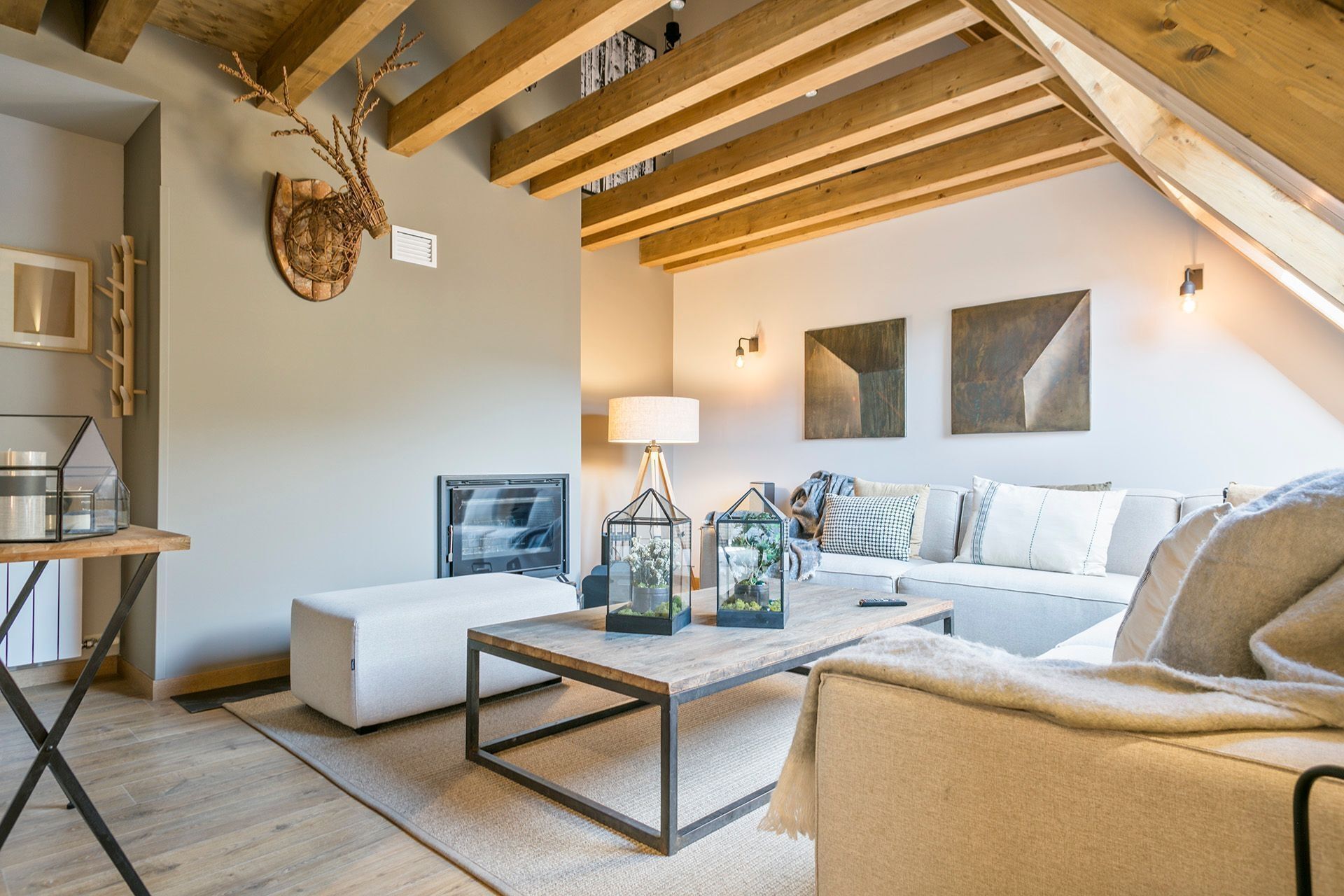 Ein gemütliches Wohnzimmer mit Holzbalkendecke, einem weißen Sofa, einem Couchtisch mit Dekoration und einem Fernseher auf einem Schrank.
