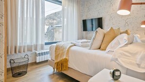 A bedroom with a bed, a bedside table, a lamp, a TV, and a window with curtains. - Luderna - Casa Peregrí (Arties)