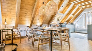 A cozy dining area with a wooden table and chairs, a hanging light fixture, and a view of the outdoors through large windows. - Luderna - Casa Peregrí (Arties)