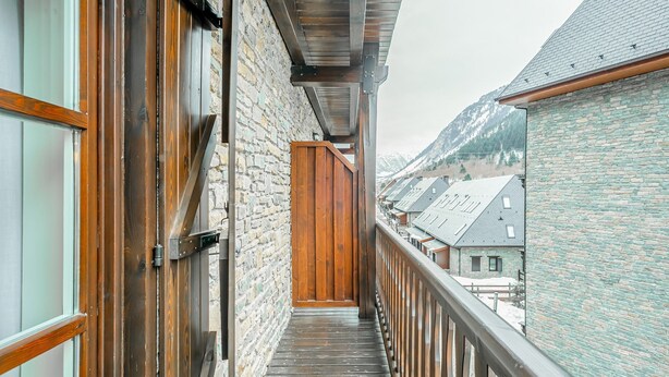 Ein schmaler Holzbalkon mit Steinmauern, der zu einer Tür führt.