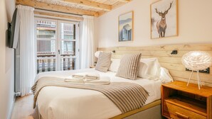 Ein Schlafzimmer mit Holzbalkendecke, einem Bett mit weißer Bettwäsche, gestreifter Bettdeko und einem Nachttisch mit Lampe.