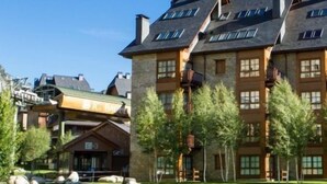 Ein mehrstöckiges Gebäude mit einer steinernen Fassade, mehreren Schornsteinen und einem gepflegten Rasen mit Steinen und Bäumen.