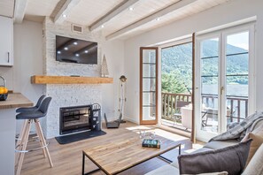 Ein modernes Wohnzimmer mit Kamin, Fernseher an einer Steinwand und einer großen Schiebeglastür, die auf einen Balkon mit Bergblick führt.