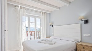 A bedroom with a bed, a nightstand, a wall-mounted lamp, and a view through a window. - Luderna - Apartamento con terraza Mirador Salardu (Naut Aran)