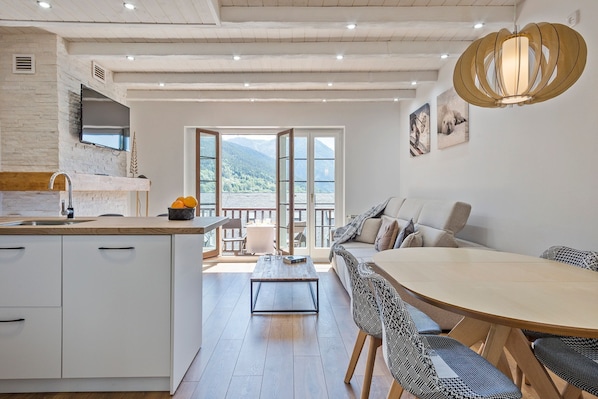 A modern kitchen with a wooden countertop, white cabinets, and a large window offering a mountain view.