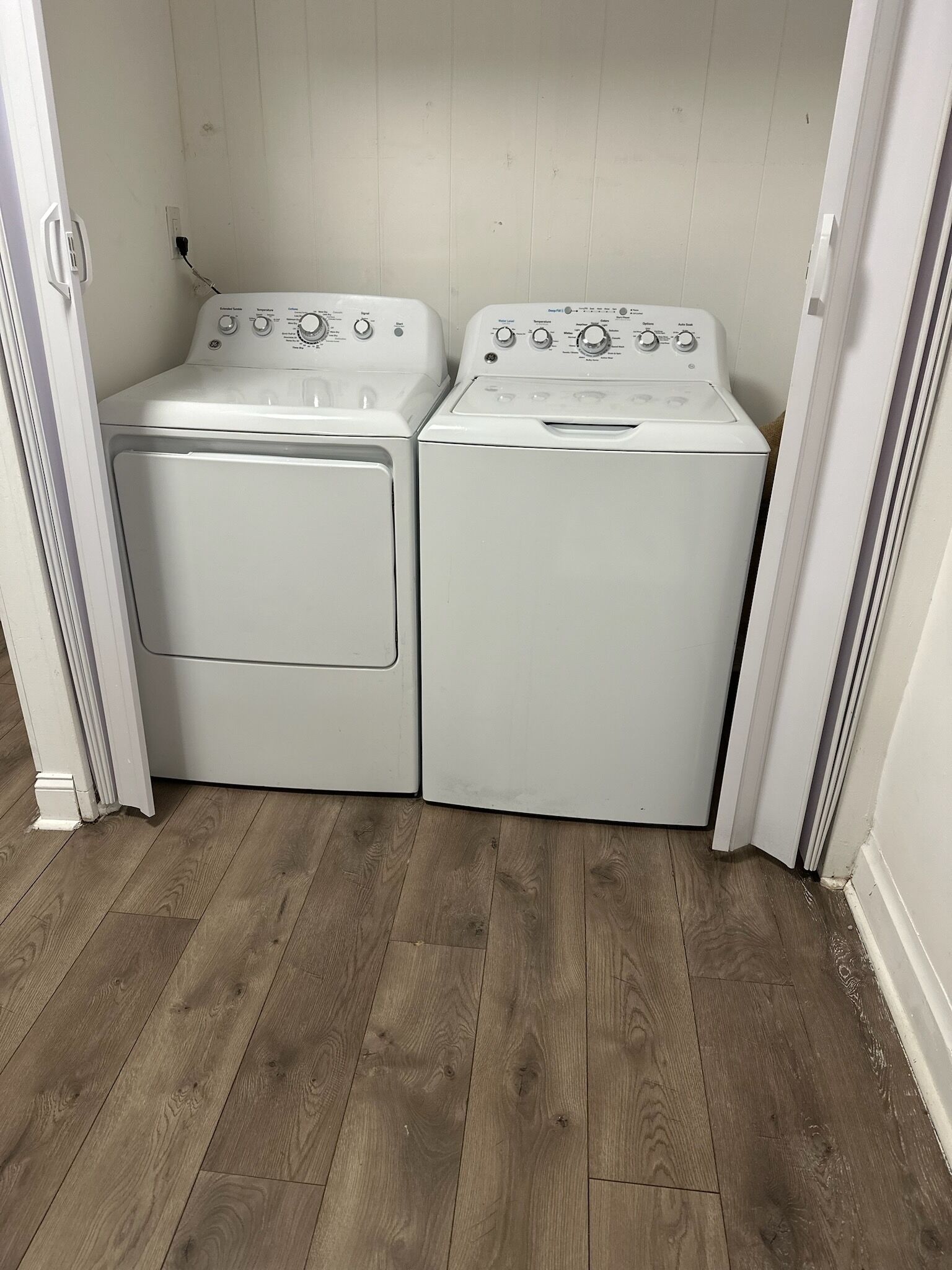 A laundry room with two stacked washers and dryers, wooden flooring, and white walls.
