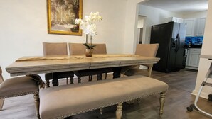 Un comedor con una mesa de madera, sillas acolchadas y un banco. Un jarrón con flores está sobre la mesa.
