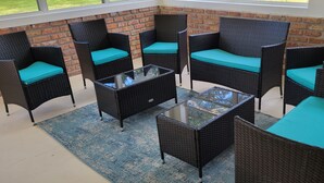 Un patio con mobiliario de mimbre y una mesa de vidrio, frente a un muro de ladrillo.
