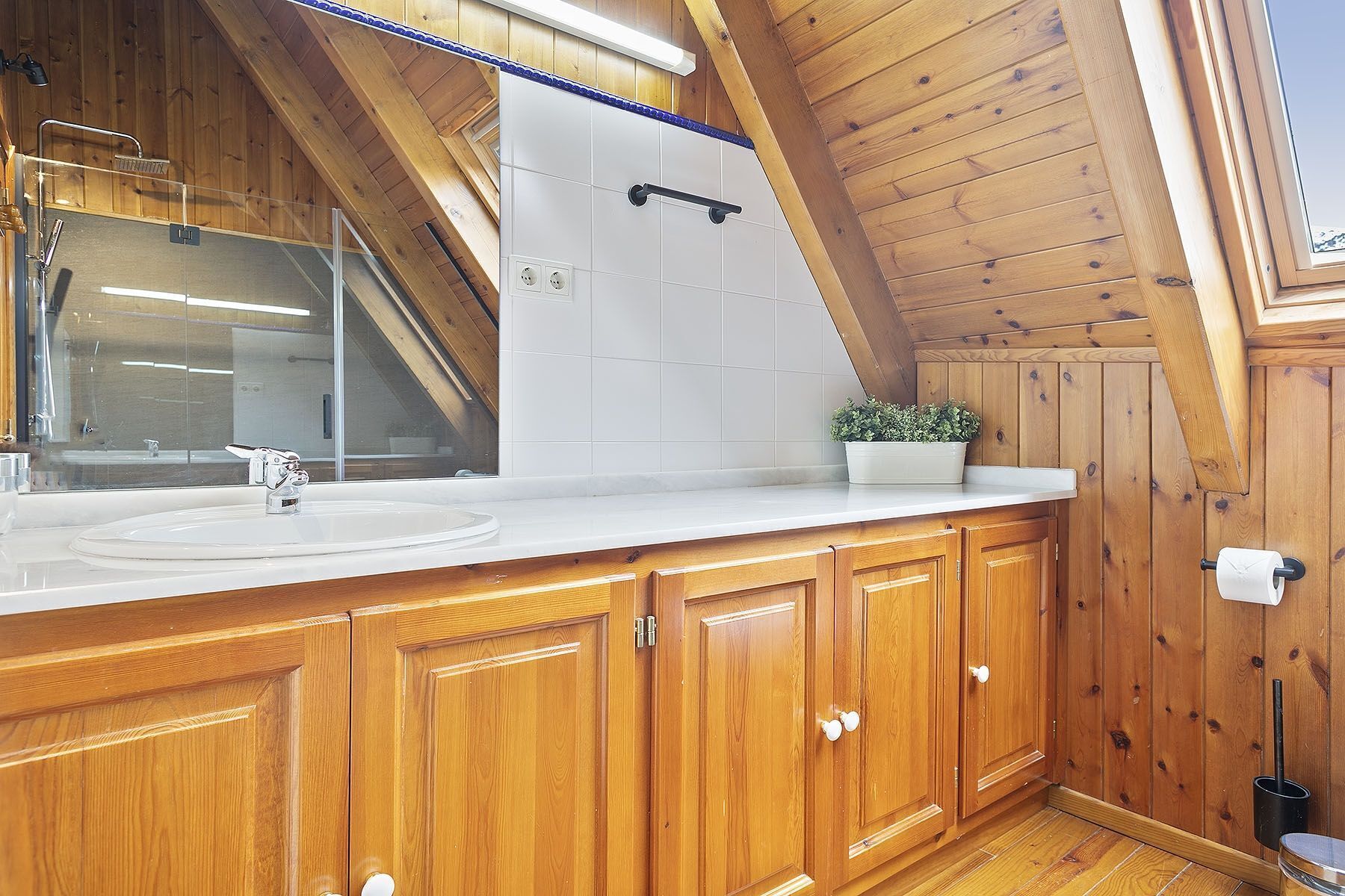 A wooden cabin bathroom with a white sink, wooden cabinets, and a skylight.