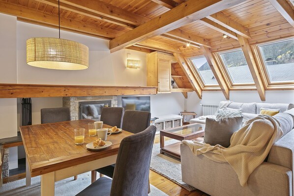Een gezellige loft met een eethoek, een open haard en een groot raam met uitzicht op de natuur.