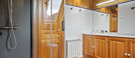 A modern bathroom with a glass shower enclosure, wooden cabinets, and a large mirror above the sink.