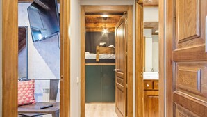 A narrow hallway with wooden doors leading to a bedroom with a bunk bed and a bathroom with a sink and mirror. - Luderna - Tríplex Val de Ruda E3 der Humarau (Baqueira)