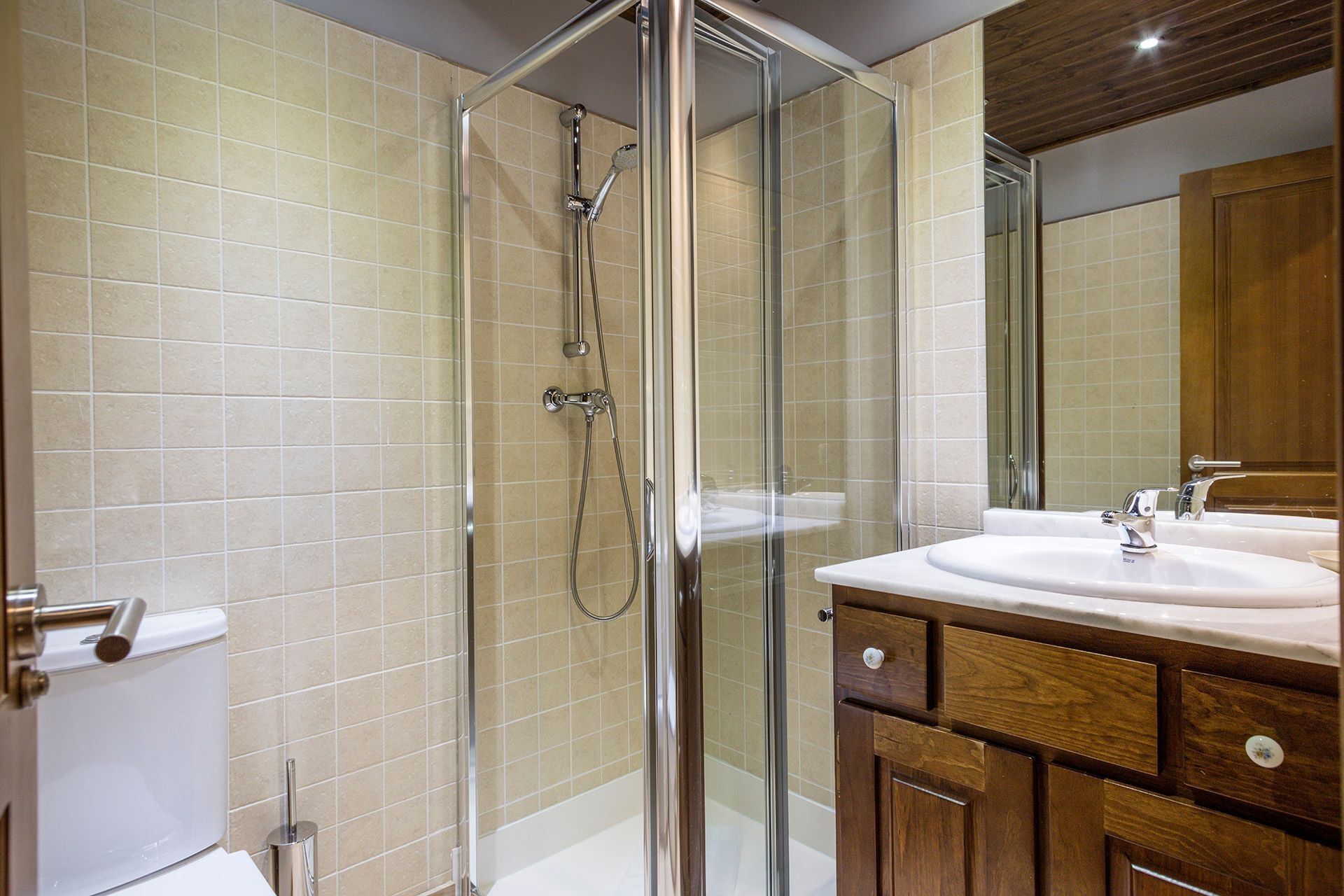 A modern bathroom with a glass-enclosed shower, a white sink, and wooden cabinetry.