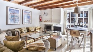 Uma sala de estar com lareira, uma área de jantar e uma janela grande com cortinas.