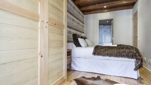Quarto com piso de madeira, cama com roupa de cama branca, manta de pele e tapete de couro.
