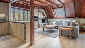 A spacious loft with a kitchen, dining area, and living room. It features wooden beams, a stone fireplace, and large windows.
